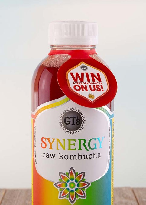 Close-up photo of a GT's Synergy Raw Kombucha bottle with a "Win a Year of Kombucha" ElastiTag hang tag. 