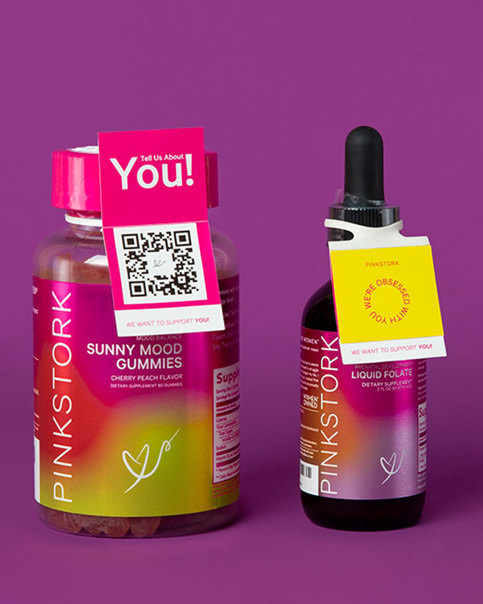 Pinkstork gummies and liquid folate bottles with tags. "Tell Us About You!" and "We're Obsessed With You" ElastiTags. Purple background.