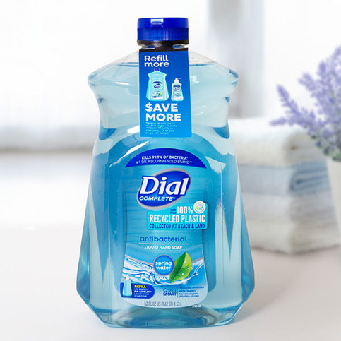 Dial Complete antibacterial hand soap bottle with "100% Recycled Plastic" label and "Save More" tag. Blue liquid, white background.