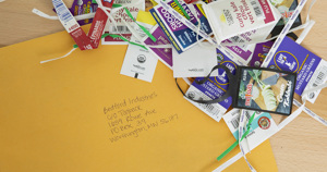 A yellow envelope with a handwritten address, surrounded by a pile of colorful twist ties and produce labels. The envelope is addressed to Bedford Industries in Worthington, MN.