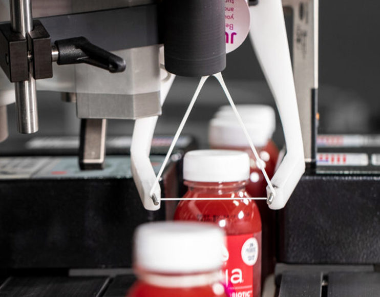 Red juice bottles running through mechanical assembly line to have ElastiTags applied by machinery.