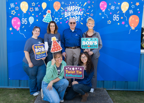 5 women pose around an older man with Photo Booth props and blue backdrop "happy birthday Bob!"
