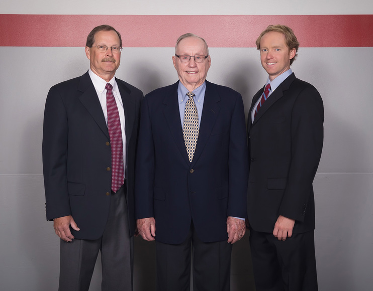 A family of three men of different generations pose together in suits and ties.