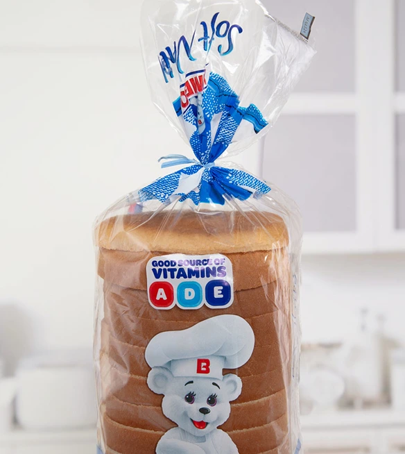 A loaf of white bread with "Good Source of Vitamins A, D, E" advertised on the bag closed by a light blue twist tie with a light kitchen background.