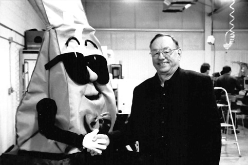 A black and white photo of a man shaking a hand of a cartoonish-character of a coffee bag with sunglasses. 