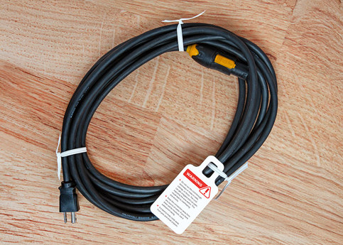 A coiled black extension cord with a warning Ring Tag label attached to the white twist tie. The label has a red exclamation point and lists safety precautions.
