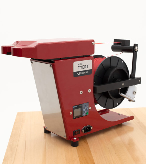 Small, red twist tying machine on a butcher's block countertop. 