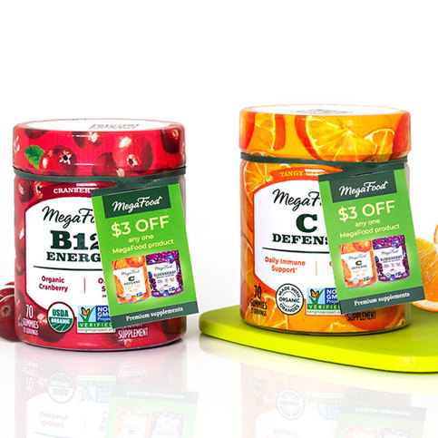 MegaFood B12 Energy and C Defend gummies with $3 off ElastiTag hangtags. Cranberry and orange flavors, on a green surface.