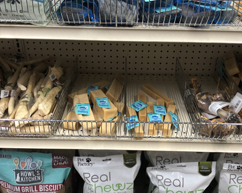 A variety of dog bones and treats on a store shelf. The dog bones have teal ElastiTags as pet treat labels.