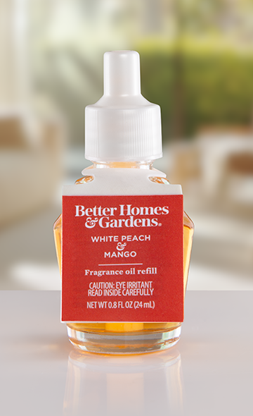 Better Homes & Gardens fragrance oil refill bottle. The ElastiTag label is red with white text and features the brand logo and scent name. The bottle contains a yellow liquid.