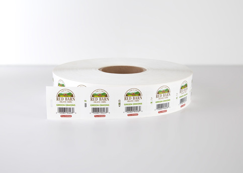 A spool of white TagTie labels with "Red Barn Organic Farms Green Onions" and a barcode, on a white surface.