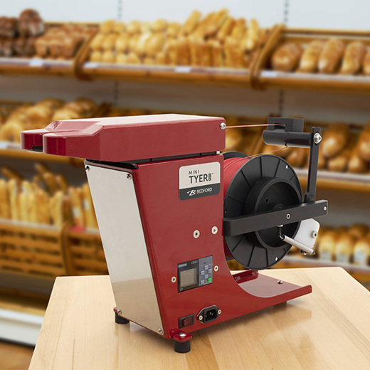 Red Mini Tyer Pro twist tying machine with baked goods in the background. 