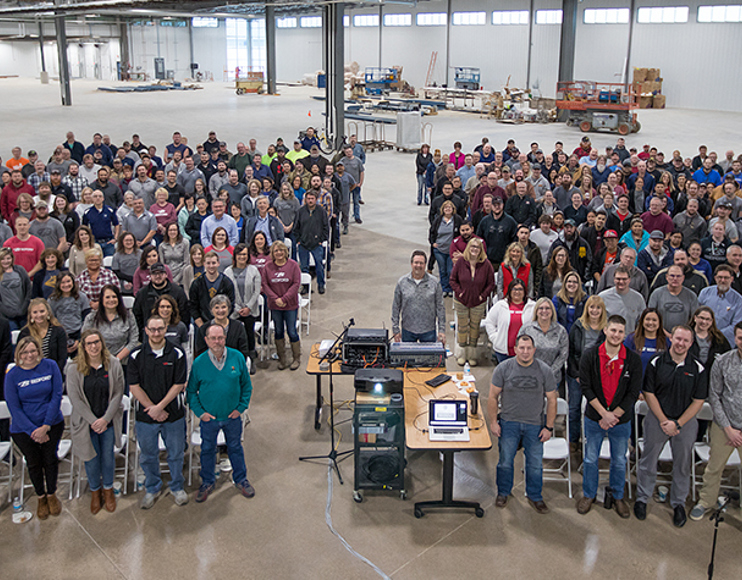 A large group of Bedford Employees pose for a photo in an empty manufacturing floor. 