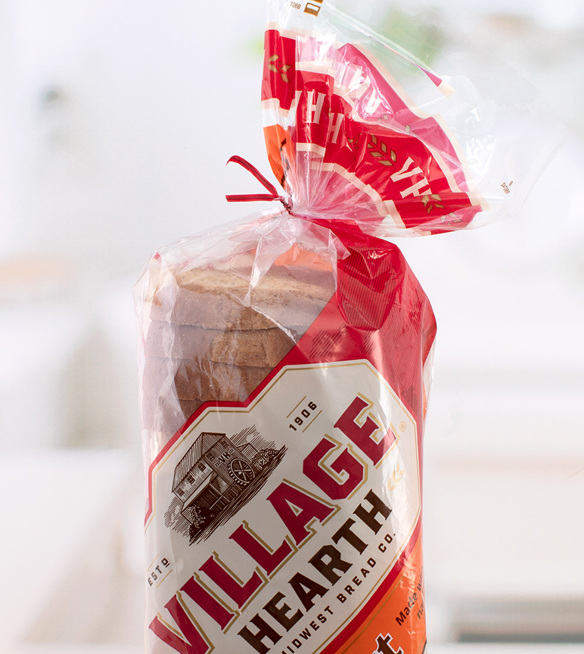 A red bread tie closes a bag of Village Hearth brand honey wheat bread.