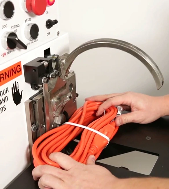 Bedford ring tier machine applying twist tie to orange extension cord.