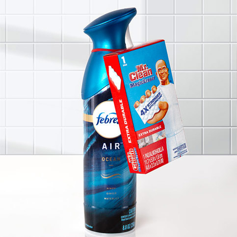 Febreze Air Ocean spray can with Mr. Clean Magic Eraser box attached by a red ElastiTag tote. On a white tiled background.