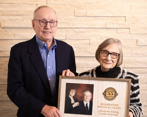 An older man and woman with a plaque that signifies "celebrating 55 years of innovative thinking and stellar leadership." 