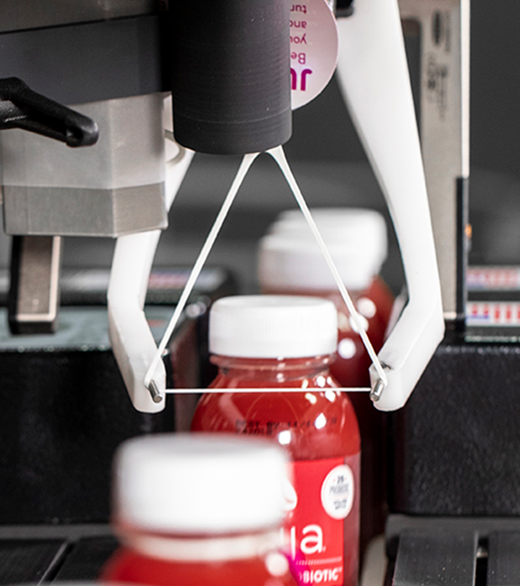 Red juice bottles running through mechanical assembly line to have ElastiTags applied by machinery.