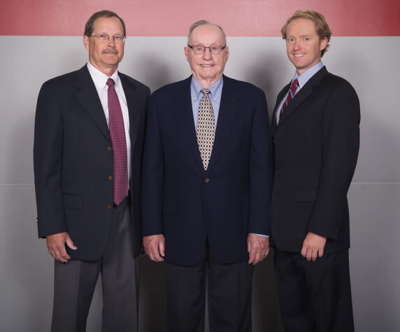 A family of three men of different generations pose together in suits and ties.