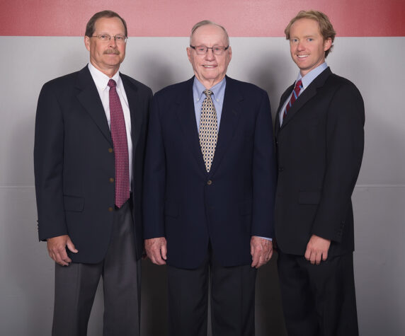 A family of three men of different generations pose together in suits and ties. A family of three men of different generations pose together in suits and ties.