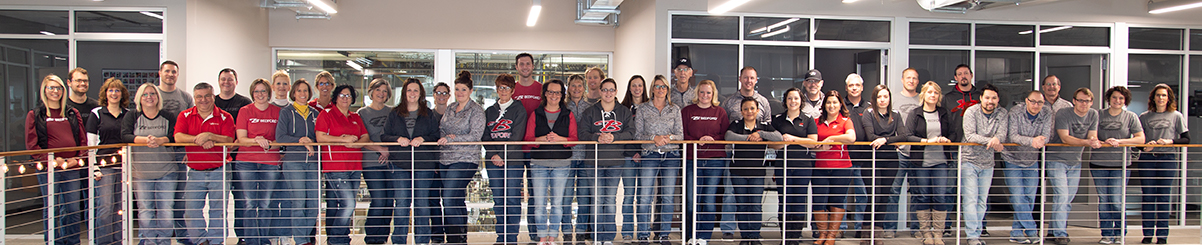 A large group of Bedford employees in Bedford-branded attire pose for a photo on a balcony