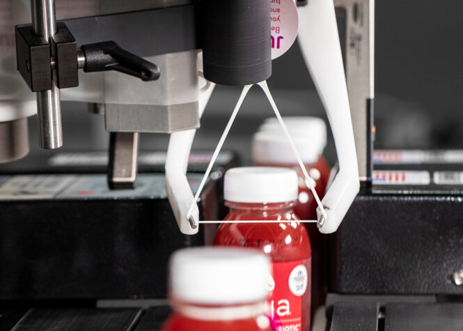 Red juice bottles running through mechanical assembly line to have ElastiTags applied by machinery.