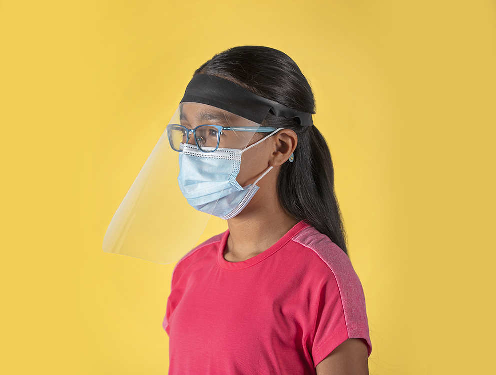 A young girl wearing glasses and a face mask models a clear face shield manufactured by Bedford Industries