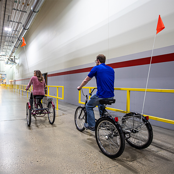 A man and a woman pedal bicycles in a manufacturing facility