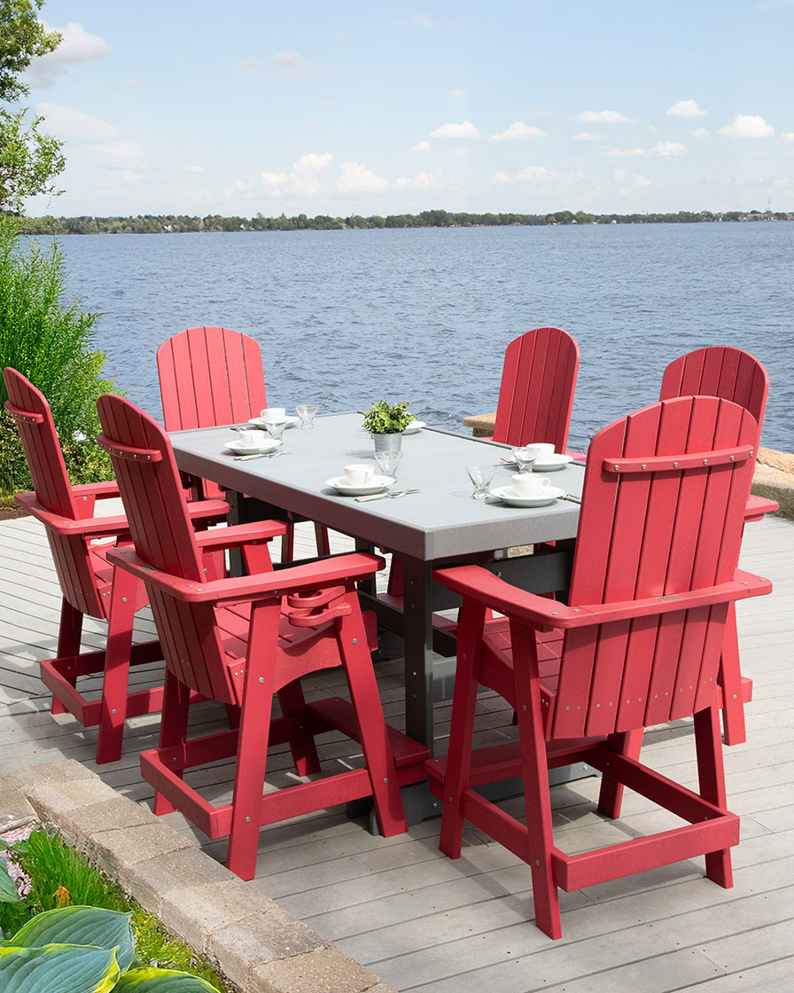 Red outdoor dining set with made of recycled plastic lumber with a gray tabletop and six chairs on a wooden deck near a body of water.